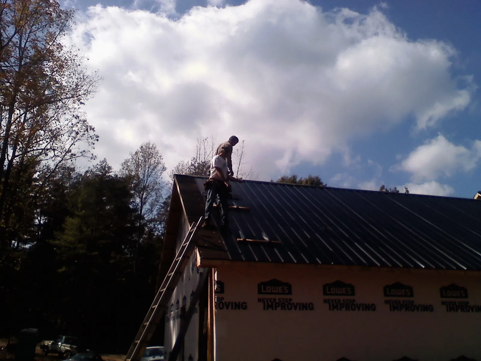 Roofer fastening dark metal panels high against a cloudy sky, from a Roof Inspection job in Paragonah