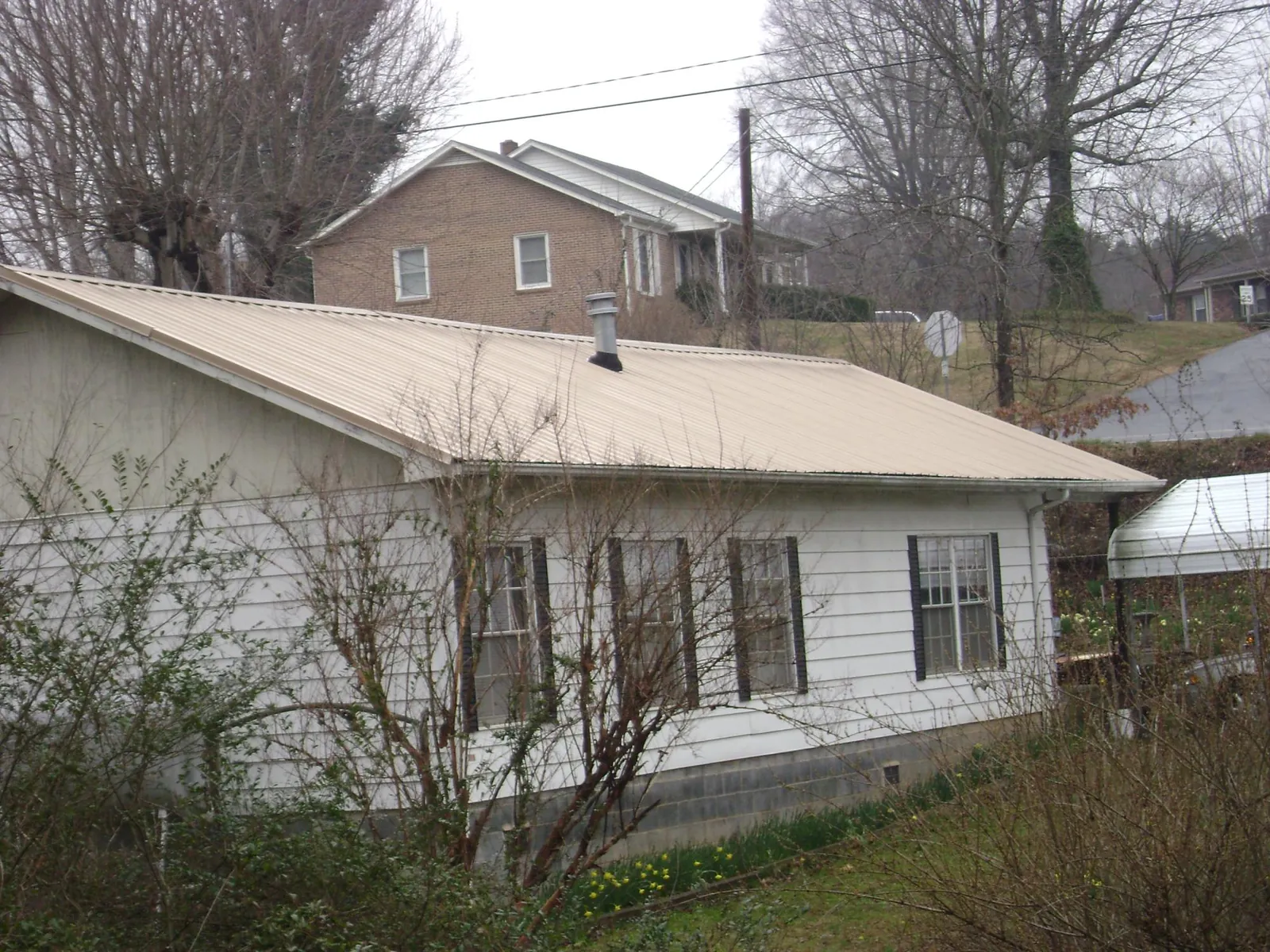 Tan metal roof on a white sided house set into a hillside — Commercial Roofing by Roofing Brothers in Paragonah